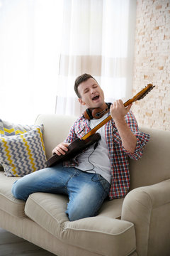 Young man in headphone enthusiastically playing the electric guitar in a light room