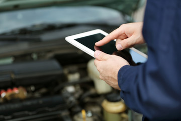 Mechanic standing in front of an open car hood with the tablet