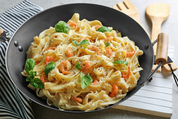 Pan with tasty alfredo pasta, kitchen board, napkin, spoon and fork on grey table