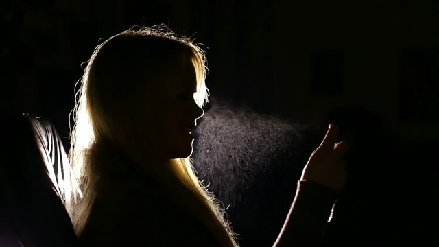 Beautiful girl spraying perfumes close-up indoors. Close-up silhouette in shadow of a woman hands holding perfume.