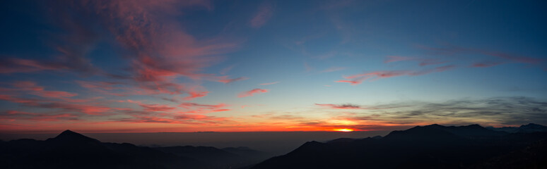 Fiery sunset from mountain pick with thin glazes in the sky evening. Fall season. Orobie alps. Rena pick. Bergamo Italy. In the distance the Monviso.