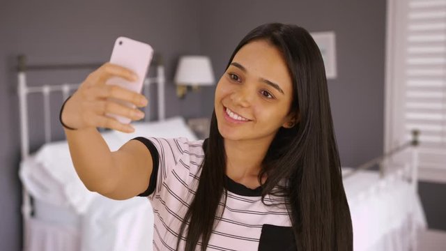 A cute teen takes a selfie in her bedroom. A young girl takes a picture of herself with her smart phone. 