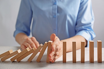 Businesswoman hand trying to stop toppling dominoes on table