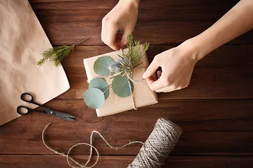 Photo sur Plexiglas Fleuriste Mains féminines faisant une boîte-cadeau avec des fleurs sur une table en bois