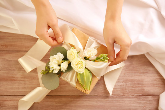 Female hands making gift box with flowers on wooden table