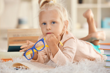 Small girl with glasses with many books on carpet