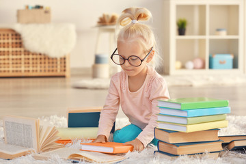 Small girl in glasses with many books on carpet