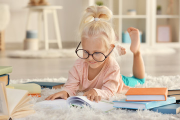 Small girl in glasses with many books on carpet