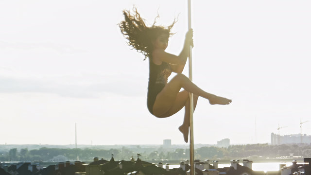 Fit attractive girl poledancer hanging on the pole at summer day portable dancing stage over the skyline, telephoto