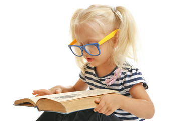 Cute small girl in glasses reading book on white background