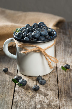 Fresh blueberries in enameled cup, rustic background, selective focus