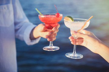Male and female hands holding glasses with margarita cocktail on blurred background