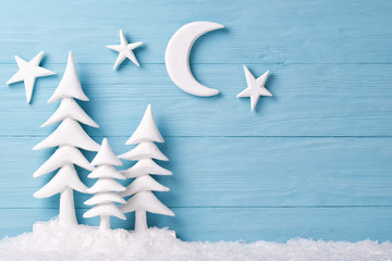 Christmas background with white christmas trees, snow, moon and stars, blue wooden background