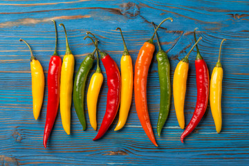 Fresh colored chili peppers on blue wooden background