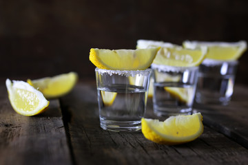 stack of tequila with salt and lemon on a wooden background