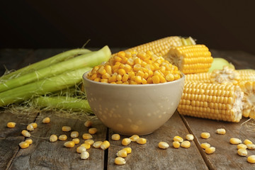 Bowl with corn seeds and ripe corn cobs on wooden table