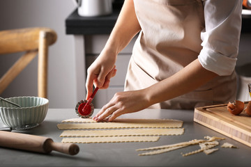 Woman cutting dough for ravioli on table