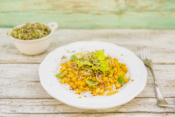 Salad with cooked peas and fresh sprouts with herbs on wooden table.