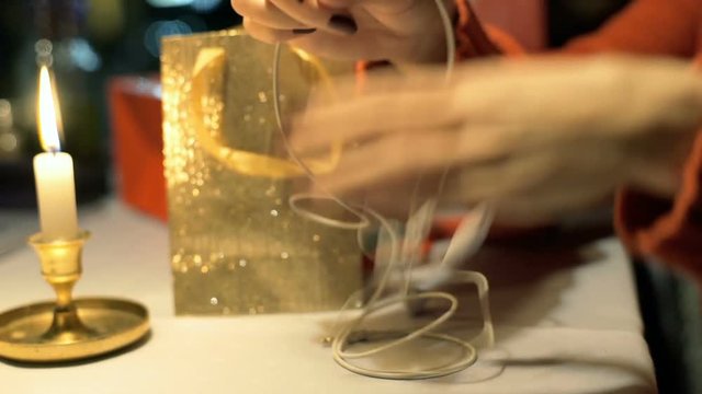 Girl tries to untangle earphones while sitting by the table at night

