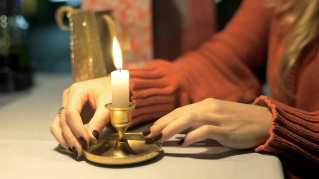 Girl moves the burning candle and snuffs it out while sitting in the cafe
