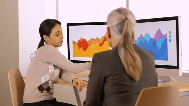 Two office professionals talk about their company's statistics. Businesswomen talk about their work. 