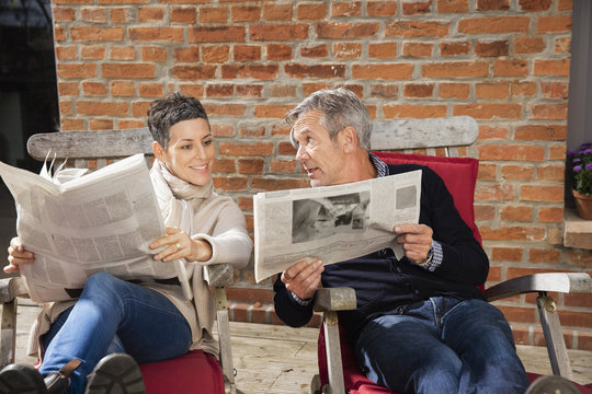 Man showing newspaper to happy woman while sitting in back yard