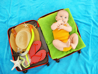 Cute baby and things for vacation in suitcase lying on blue bedspread. Holidays at sea with baby,...
