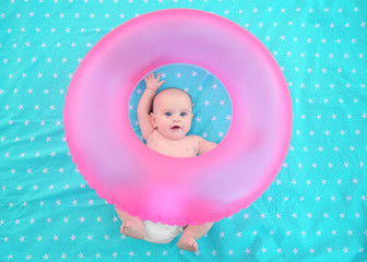 Cute baby with pink swim ring lying on bedspread. Holidays at sea with baby, concept