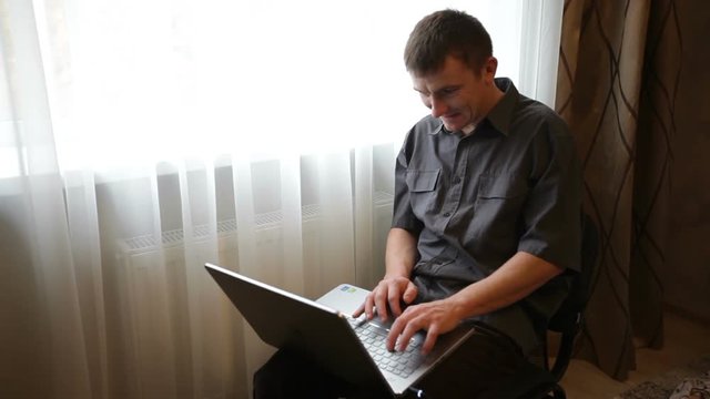 young man sits at a laptop and plays the game