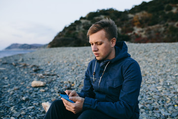 man sitting on the beach and using a cell phone
