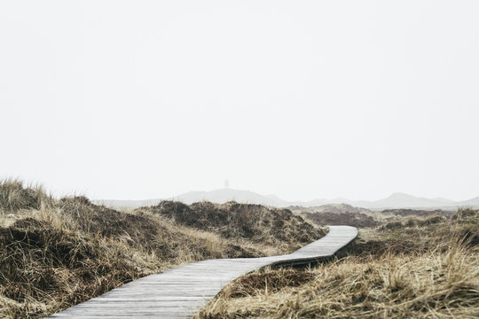Boardwalk on field against sky in foggy weather