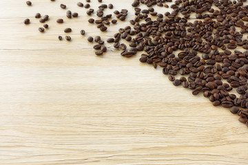 Fresh roasted coffee beans spread out towards the light on brown wooden background with lots of copy space.