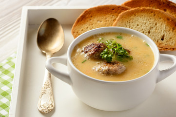 Vegetable cream soup with meatballs on white wooden background.