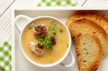 Vegetable cream soup with meatballs on white wooden background.