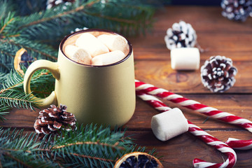 Close view at mug with hot chocolate, christmas tree, tangerines, peppermint stick and marshmallow on a wooden background. Dark photo. Empty space for text. Toned for art effect