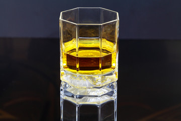 Glass with whisky drink on glass surface