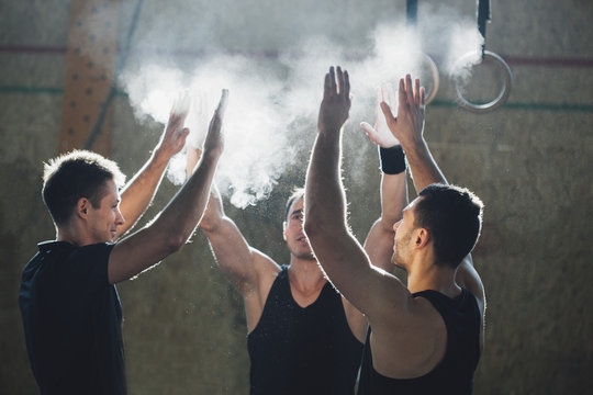 Determined male athletes dusting sports chalk together at gym