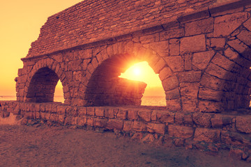 Remains of the ancient Roman aqueduct in ancient city Caesarea at sunset. Israel.