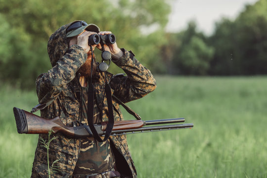 Hunter looking through binoculars on grassy field