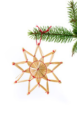juldekoration halm stjärna som hänger i grankvist med vit bakgrund