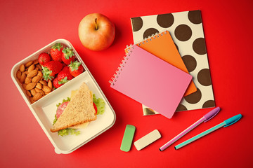 Lunch box with food and stationery on red background, top view