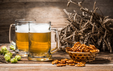 Fototapeta premium Photo of two mugs, beer with pretzels, wheat spikes, hops