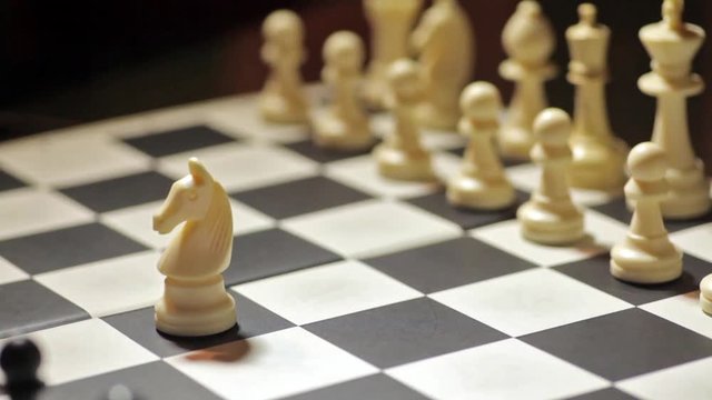 Color footage of a chess match, with white knight capturing the black pawn.