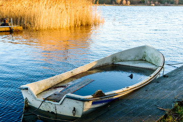 Small water filled rowboat moored beside a narrow wooden pier on a cold winter morning. Ice inside the boat.