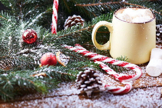 mug with hot chocolate, christmas tree, tangerines, peppermint stick and marshmallow on a snow wooden background with falling snow. Dark photo. Empty space for text. Selective focus