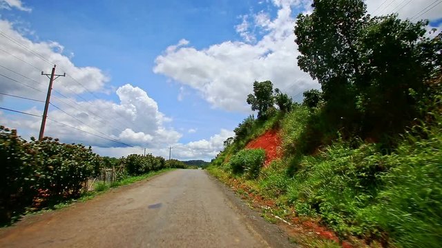 motion along country road to horizon past scooter between plants hilly ground slopes against blue sky with white clouds