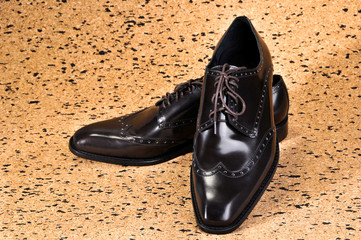 Men's Classic Leather Shoes designed with a slim elongated toe, made from a smooth brown leather. standing on a sheet of balsa wood