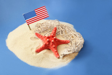 USA flag, starfish and net in sand on blue background. Columbus Day concept