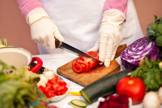 Woman with gloves cutting tomato with a knife