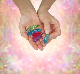 Crystal Therapist Holding Aura Terminated Quartz Wands - female crystal therapist holding and offering a  selection of brightly colored aura quartz wands on a pink and orange sparkling background 